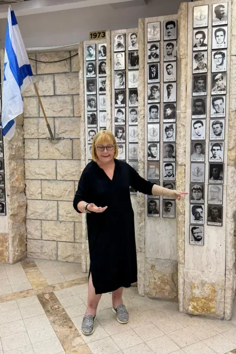 Oren Rosenfeld/BBC Dorit Barak gestures next to a memorial in Bnei Brak to local soldiers who were killed in battle during Israel’s wars